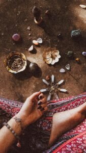 A woman's hand in a spiritual ritual with crystals, incense, and natural elements.